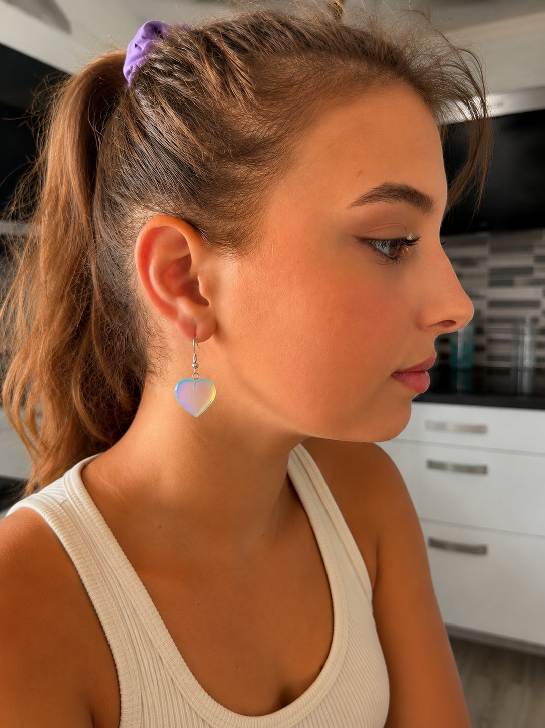 Jeune femme portant des boucles d'oreilles La boutique d'Emma en forme de cœur irisé avec monture en métal argenté
