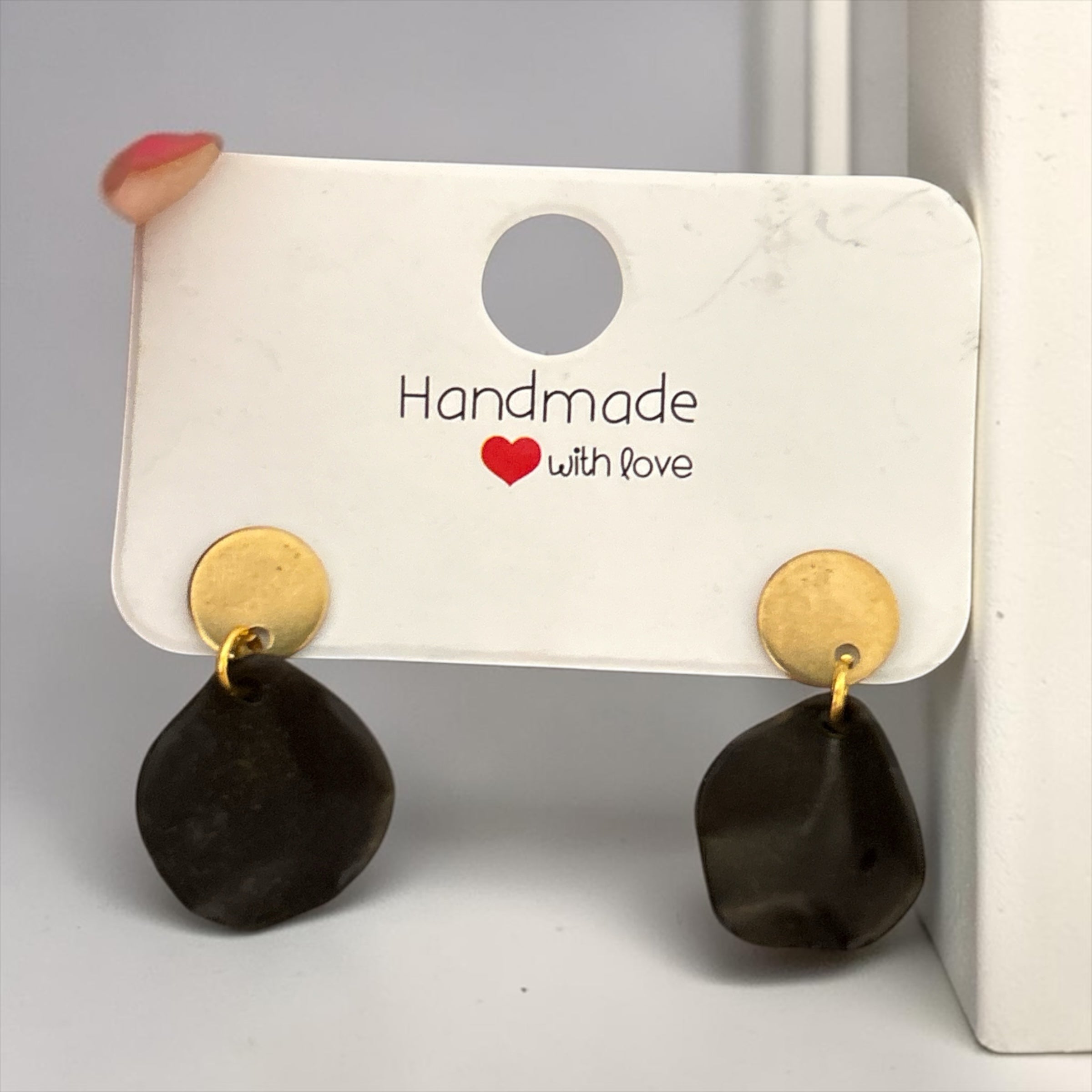 Boucles d'oreilles La boutique d'Emma artisanales avec disque doré et pendant noir organique sur support blanc