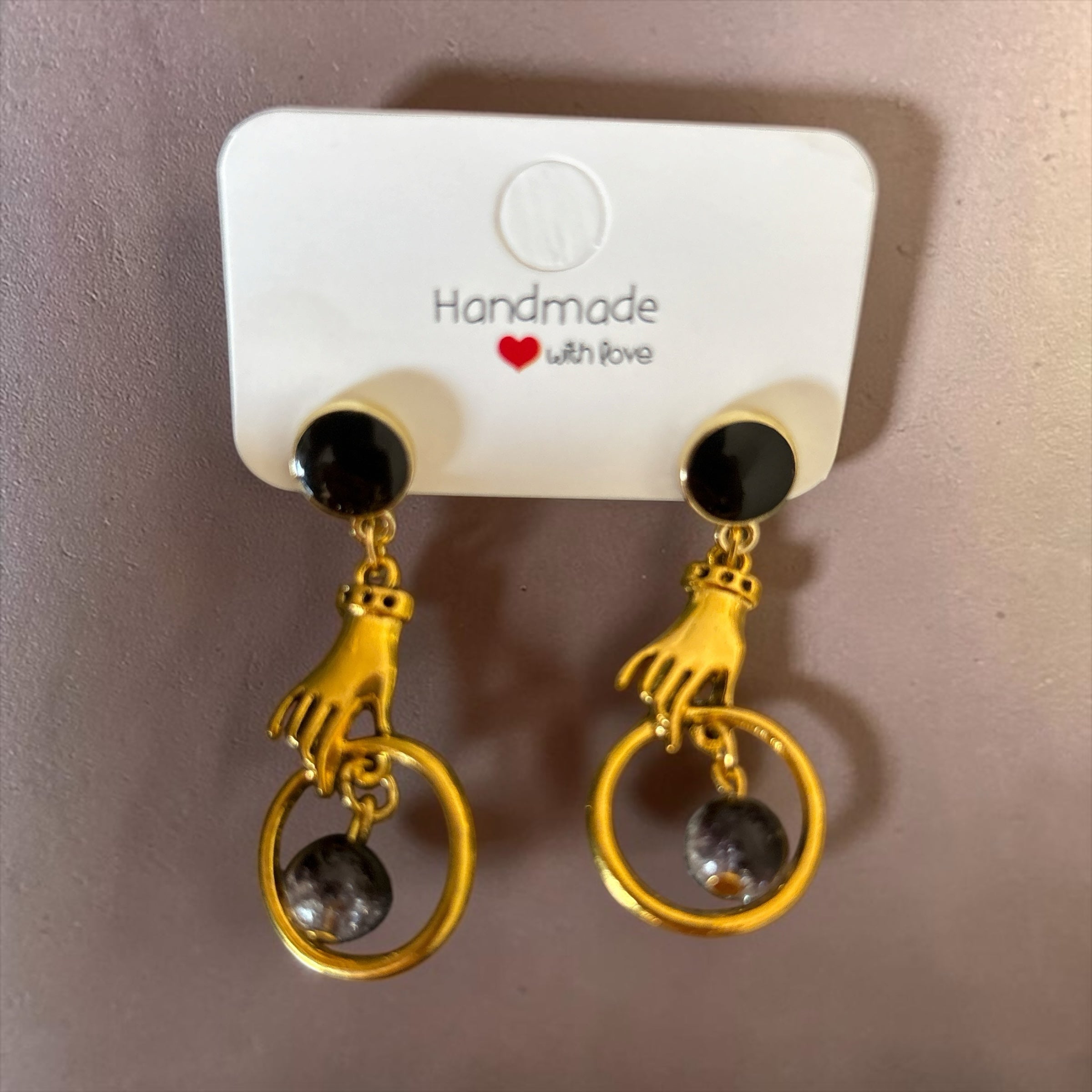 Boucles d'oreilles La boutique d'Emma dorées avec motif main tenant un anneau et perle sombre sur clou noir
