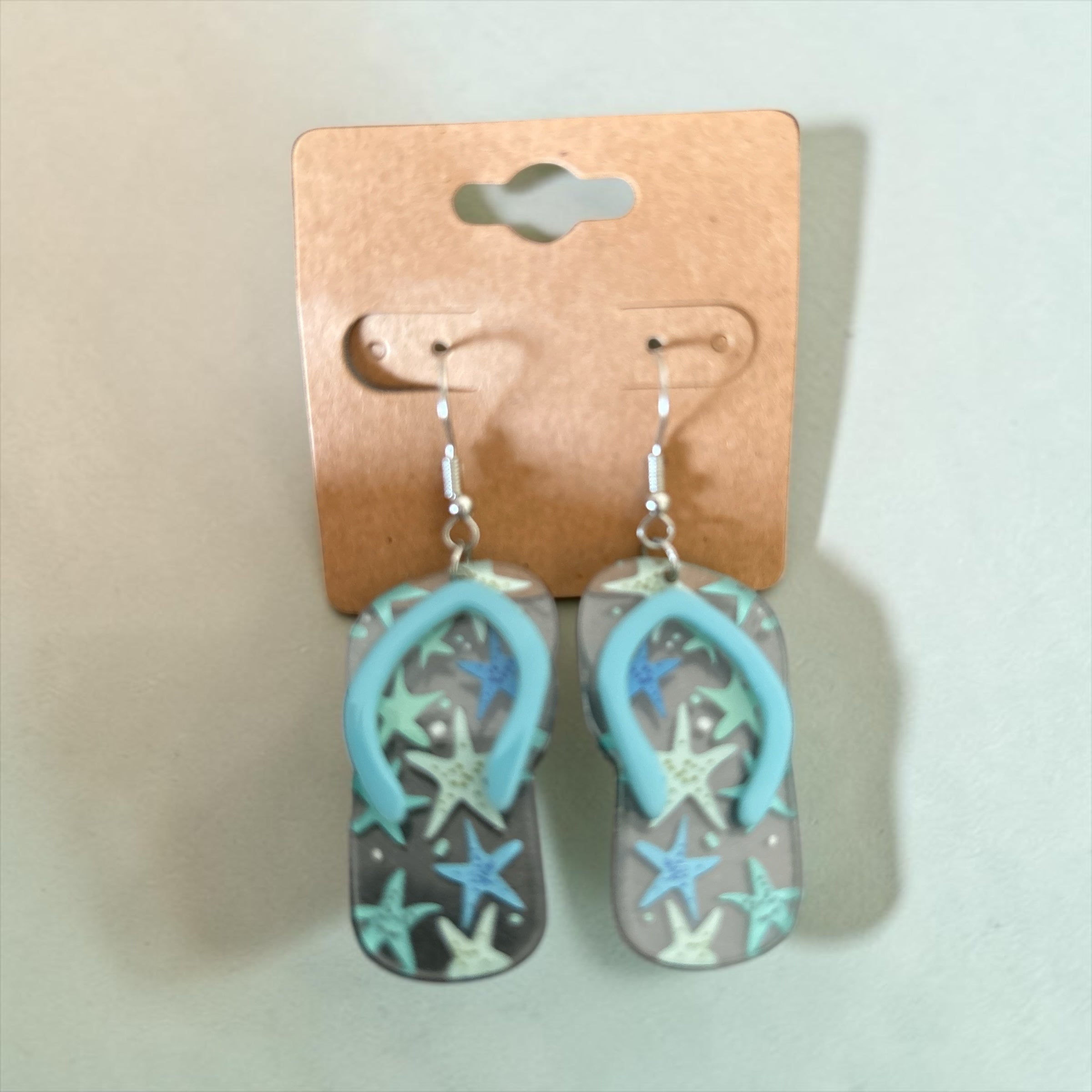 Boucles d'oreilles La boutique d'Emma en forme de tongs translucides avec motif étoiles de mer bleu et turquoise.