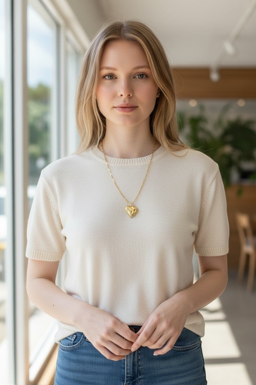 Femme portant un collier pendentif cœur texturé en plaqué or de La boutique d'Emma sur un pull beige.